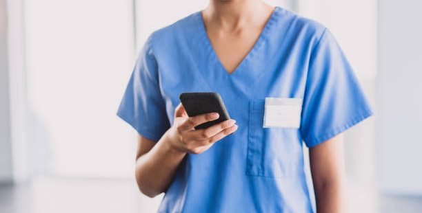 Cropped shot of an unrecognizable nurse using a cellphone while standing in her office during the day