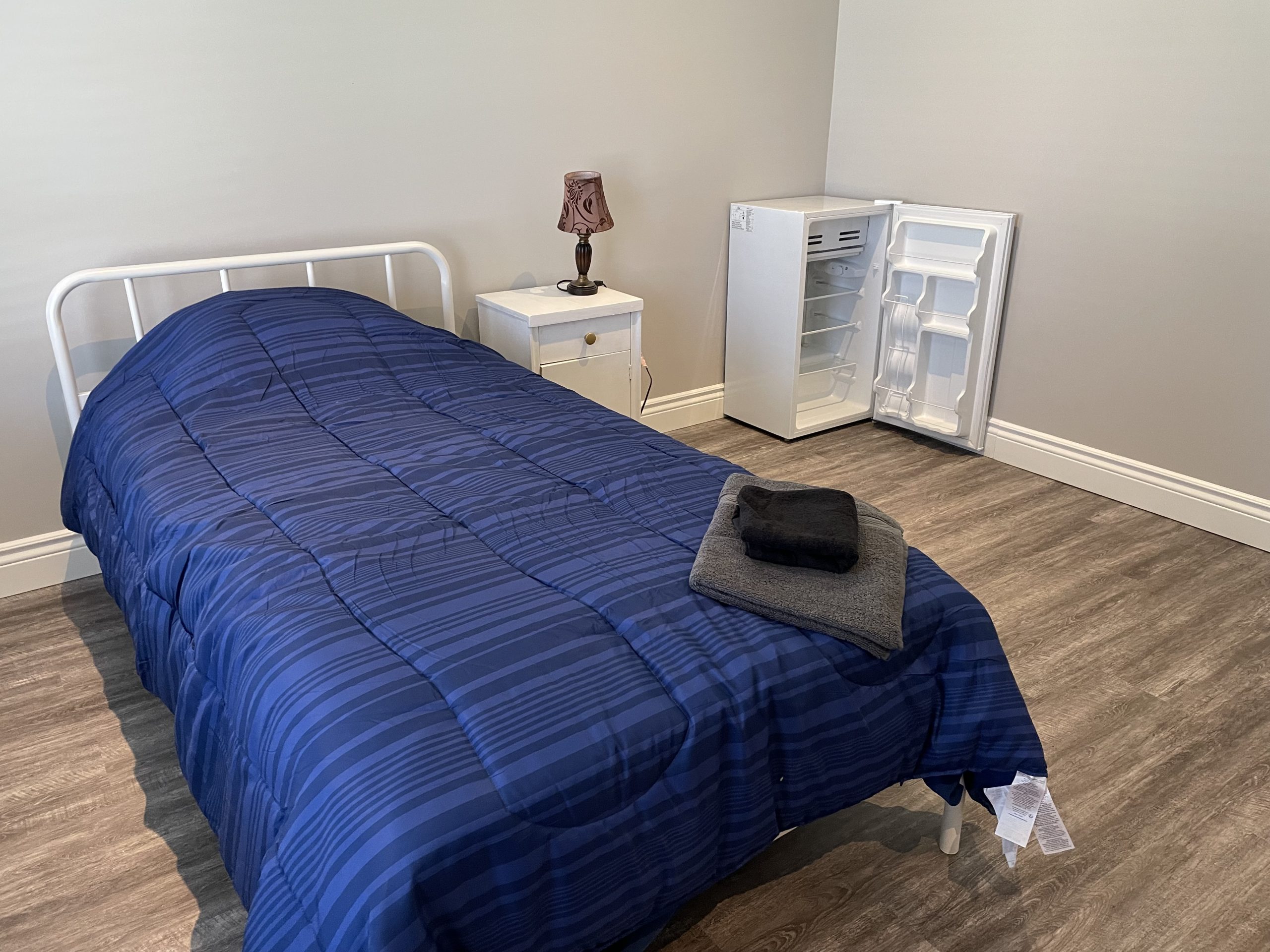 One of the bedrooms at the Light House with a bed, nightstand, and mini fridge.